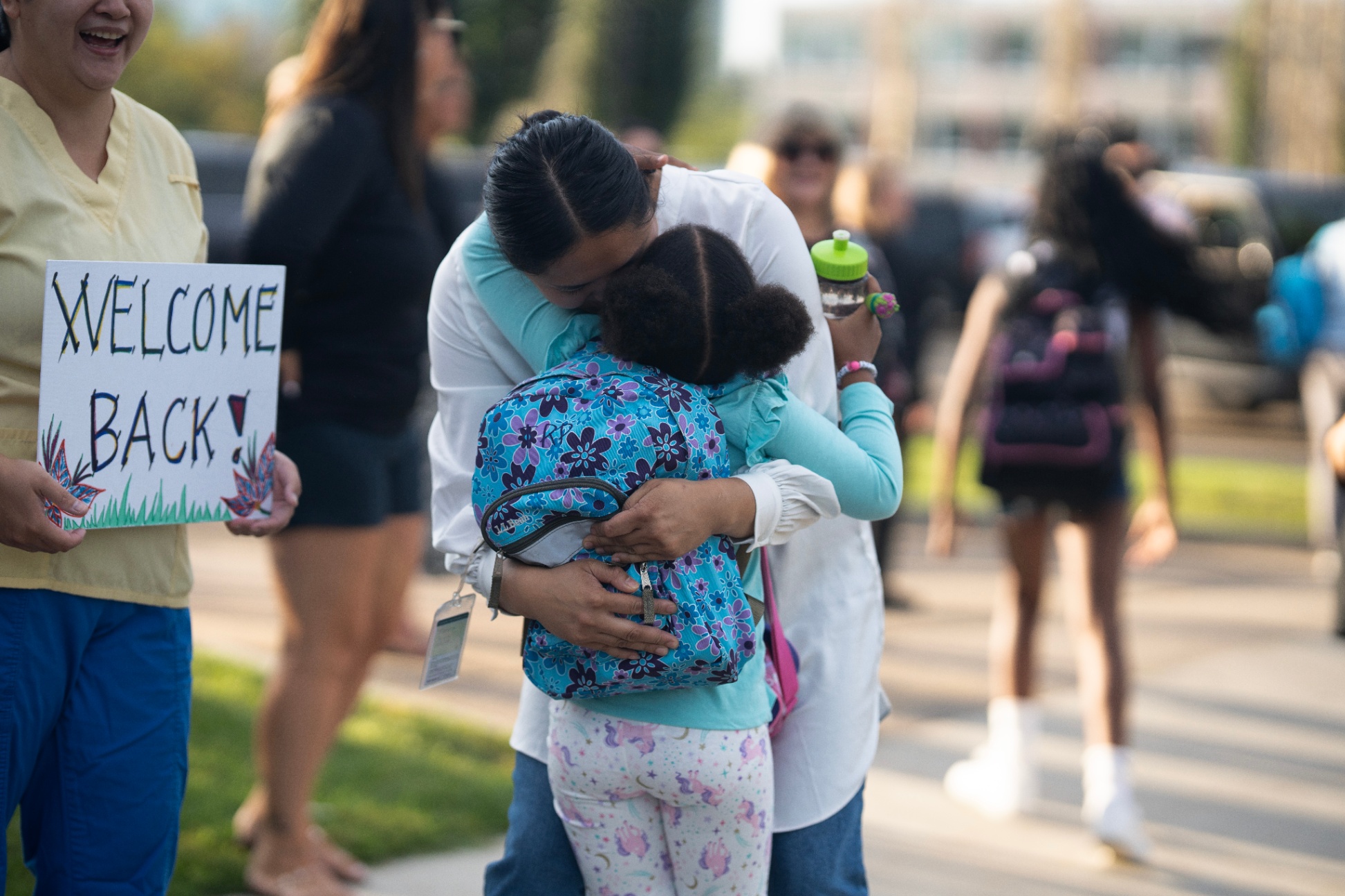 Teacher holding welcome back sign, parent hugging a child